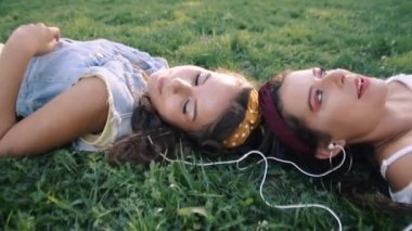 İki kız / kız kardeş çim üzerinde, kulaklık müzik dinliyor yatıyor. İki esmer parkta çimenlerin üzerinde uzanır, rahatlar, şarkı söylerler..
