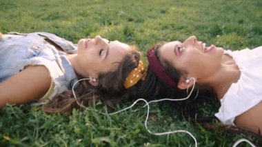 İki kız / kız kardeş çim üzerinde, kulaklık müzik dinliyor yatıyor. İki esmer parkta çimenlerin üzerinde uzanır, rahatlar, şarkı söylerler..