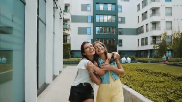 2人のガールフレンド 姉妹が新しい建物 オフィス 街の近くを歩く 女の子 歩いて ジャンプ楽しいがあります 観光客が歩いて笑う — ストック動画