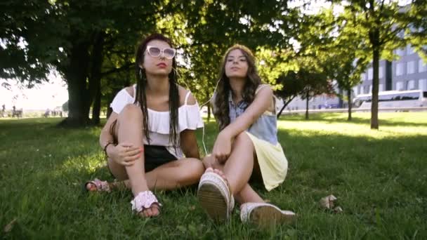 两个女朋友 姐妹躺在草地上 用耳机听音乐 两个黑发躺在公园的草地上 — 图库视频影像