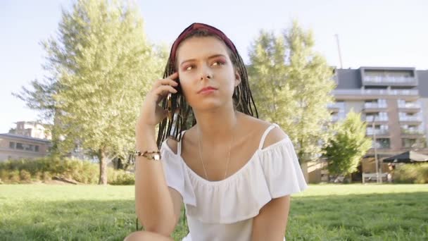 一个女孩坐在公园里 写信息 打电话 黑发女人在电话里说话 在公园里漫游 女孩给她的朋友 男朋友打电话 女孩在讲电话时面带微笑 — 图库视频影像