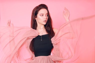 Uzun saçlı güzel esmer kız. Pembe elbiseli, uçan elbiseli, kumaşlı bir model. Pembe makyaj, tarz, moda, güzellik portresi