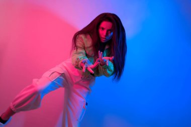 Esmer olan neon ile dans ediyor, kırmızı-mavi dansçı. Hip hop kızı, parti, gülümseme. Model uçuyor, atlıyor. Parlak fotoğraf, duygular.