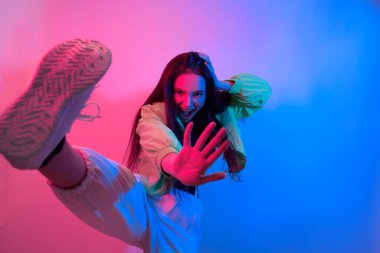 Esmer olan neon ile dans ediyor, kırmızı-mavi dansçı. Hip hop kızı, parti, gülümseme. Model uçuyor, atlıyor. Parlak fotoğraf, duygular.