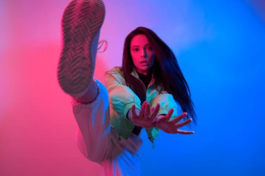 Esmer olan neon ile dans ediyor, kırmızı-mavi dansçı. Hip hop kızı, parti, gülümseme. Model uçuyor, atlıyor. Parlak fotoğraf, duygular.