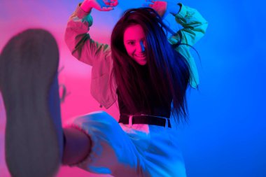 Esmer olan neon ile dans ediyor, kırmızı-mavi dansçı. Hip hop kızı, parti, gülümseme. Model uçuyor, atlıyor. Parlak fotoğraf, duygular.