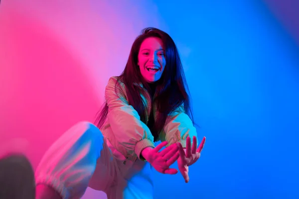 Esmer olan neon ile dans ediyor, kırmızı-mavi dansçı. Hip hop kızı, parti, gülümseme. Model uçuyor, atlıyor. Parlak fotoğraf, duygular.