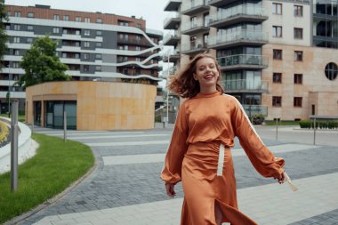 Uzun elbiseli bir kız model cadde boyunca bir yıldız gibi yürüyor. Sokakta manken gösterimi, kısa saçlı bir kızın sokak fotoğrafı. Güzel bir kadın yürüyor, gülümsüyor, şık saçlı, neşeli..