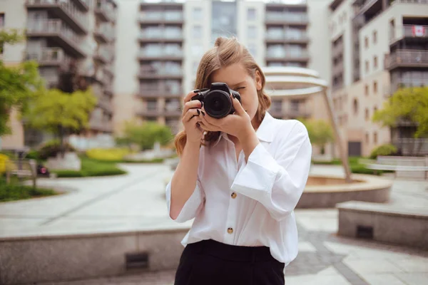 A beautiful girl looks in the viewfinder in the camera, and takes pictures. The blonde learns to photograph and earn money on the photo. A girl photographer walks around the city and takes pictures of everything around.