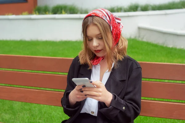 一个有着蓝眼睛 头巾和红色口红的漂亮女孩的画像 一个模特坐在街上看电话 发短信 叫出租车 — 图库照片