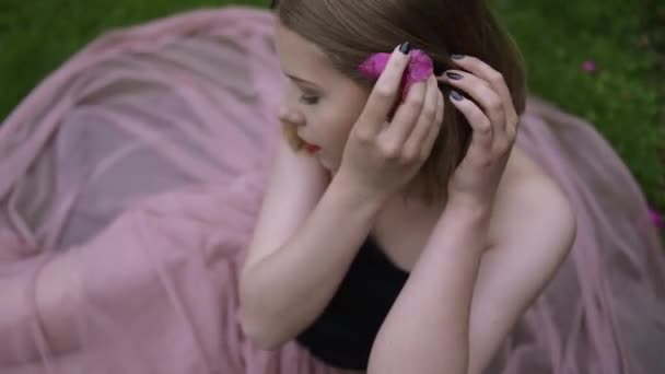 一个漂亮的女孩的画像 她的头发在花朵中 一个金发姑娘在粉色花朵的后面 一张夏天的照片 她穿着时髦的衣服 美丽的仙境 美丽的妆容 短短的头发 — 图库视频影像