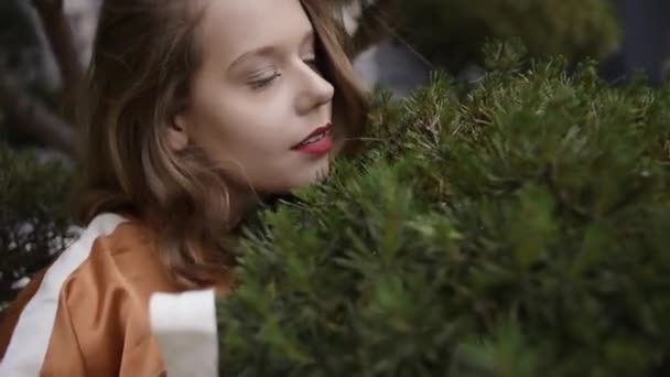 トウヒの背景に美しいモデル 短い髪と茶色のドレスの女の子 ブロンドは木の上に横たわっており モデルはファッショナブルなポーズをとっています 自然への愛 — ストック動画
