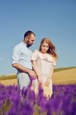 Bir çift lavanta tarlasında duruyor. Pembe elbiseli ve hasır şapkalı sarışın, mor bir çiçek tarlasının arka planında. İlişkilerde romantizm, aromalar, alerjiler ve parfümler. Çiftler burunlarını sürtüyor.