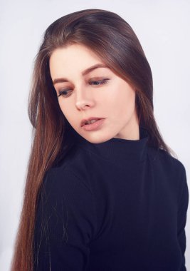 Stüdyoda beyaz arka planda poz veren esmer bir kız. Siyah balıkçı yakalı güzel bir manken.