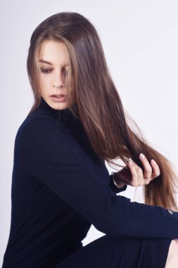 Stüdyoda beyaz arka planda poz veren esmer bir kız. Siyah balıkçı yakalı güzel bir manken.