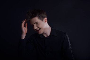 Siyah arka planda siyah gömlekli bir adamın stüdyo portresi. Avrupa görünümlü yakışıklı bir genç adam. Adam güler, iyi ruh hali içindeki adam kameraya bakar.