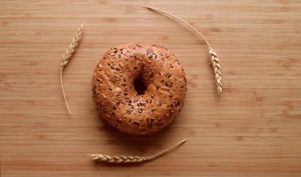 A round piece of bread, fresh pastries in a bakery. Bread with sesame seeds, cereals, seeds. Wheat ears on a wooden board. Place for text or logo, discounts