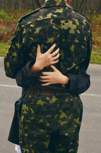 Female hands hug a man in camouflage uniform. Relations with the military, love on a melt.