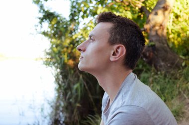 Bir adam ormanda oturur ve hapşırmak için güneşe bakar..