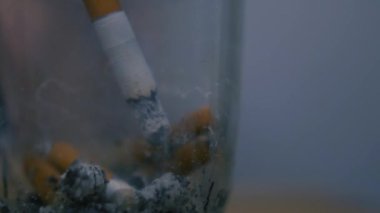 Kızın eli çakmakla bir sigara yakıyor. Yakın plan, alev, ateş. Kötü alışkanlıklar, sigara içmek. Kül tablasına kül atar, kirli kül tablasına..