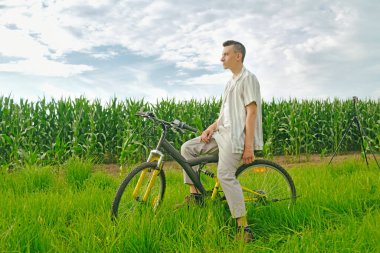 Mısır tarlasının arka planında oturan adam bir bisiklete biner.