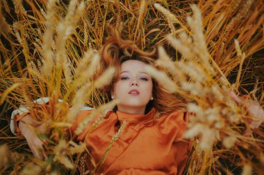 Zarif bir model buğday tarlasında uzanıyor ve doğanın tadını çıkarıyor. Doğal ürünler konsepti, doğayla bütünlük, moda. Uzun saçlı güzel sarışın kız.