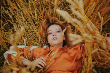 Zarif bir model buğday tarlasında uzanıyor ve doğanın tadını çıkarıyor. Doğal ürünler konsepti, doğayla bütünlük, moda. Uzun saçlı güzel sarışın kız.