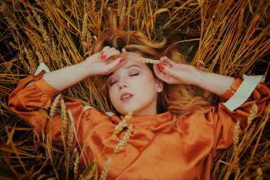 Altın buğday tarlasında bir kız elbise içinde yatıyor. Bir kadın doğada uyuyor, manken gözlerini kapadı ve temiz havanın tadını çıkarıyor.