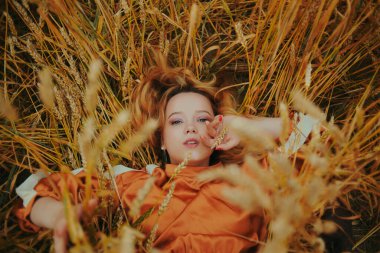 Zarif bir model buğday tarlasında uzanıyor ve doğanın tadını çıkarıyor. Doğal ürünler konsepti, doğayla bütünlük, moda. Uzun saçlı güzel sarışın kız.