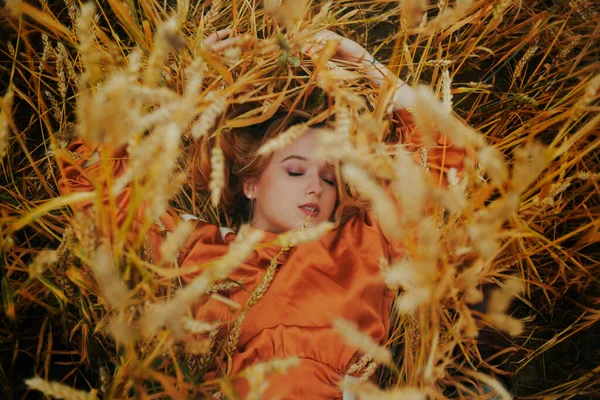A girl in a golden wheat field lies in a dress. A woman is sleeping in nature, the model has closed her eyes and enjoys fresh air