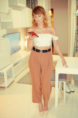 Kız dairede duruyor ve evi telefondan kontrol ediyor. Kadın ışıklandırmayı programla değiştiriyor. Akıllı Ev.