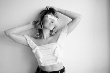 Modelin siyah-beyaz, beyaz bluzlu, gözlüklü, daha fazla küpe, bilezik ve aksesuarlı fotoğrafı.