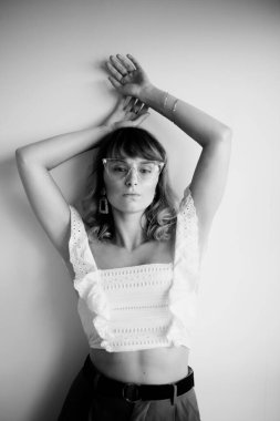 Modelin siyah-beyaz, beyaz bluzlu, gözlüklü, daha fazla küpe, bilezik ve aksesuarlı fotoğrafı.