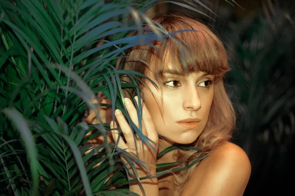 Woman in palm leaves. Model's face in green. Fashion photo of a girl in the tropics