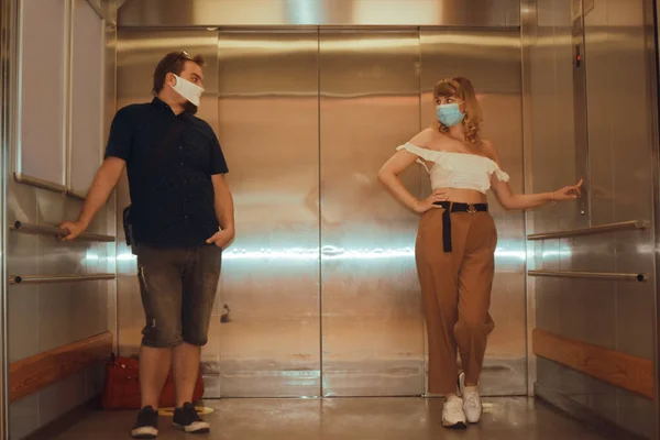 Girls and guy ride in the elevator. Students go to study. People in the elevator. Elevator with people, communication in public places. Distance 2 meters, people wearing masks