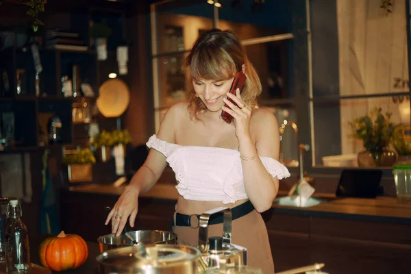 Woman preparing dinner in the kitchen. The girl speaks on the phone and prepares food. The blonde invited guests to dinner