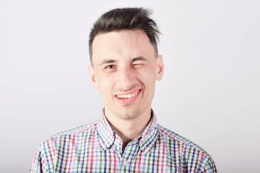 Beyaz arka plandaki çocuk gülümseyip kameraya bakıyor ve göz kırpıyor.