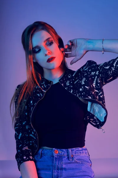 Havalı bir model. Renkli parlak ışıklar içindeki bir kadın stüdyoda poz veriyor, şık makyajlı ve manikürlü güzel bir kızın portresi. Sanat tasarımı, renkli makyaj. Renkli mavi arkaplanda.