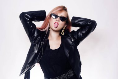 Gözlüklü pembe saçlı ve deri ceketli siyah elbiseli bir kız. Kara Cuma. Dilini gösteren kadın