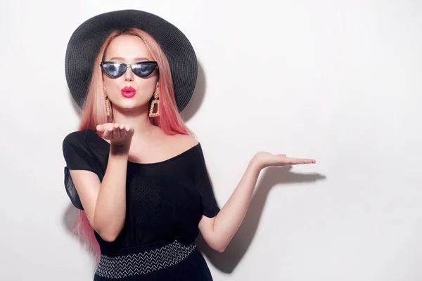 Girl with pink hair in glasses and a hat in black clothes. Black Friday. The model sends a kiss. Woman points to blank space for text