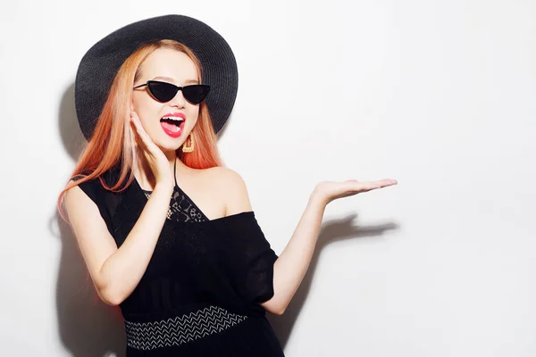 Girl with pink hair in glasses and a hat in black clothes. Black Friday. The model sends a kiss. Woman points to blank space for text