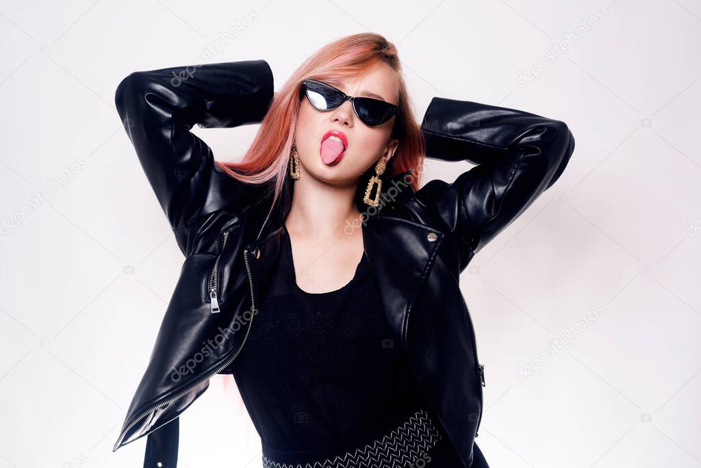 Girl with pink hair in glasses and black clothes in a leather jacket. Black Friday. Woman showing tongue