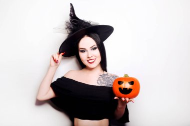 Cadı gibi giyinmiş bir kız balkabağı tutuyor. Omzunda dövmesi olan şapkalı bir manken.