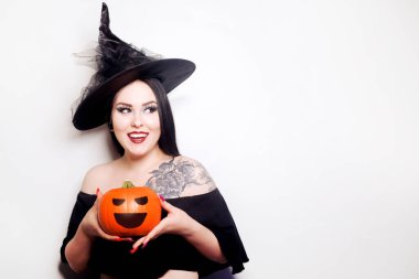 Cadı gibi giyinmiş bir kız balkabağı tutuyor. Omzunda dövmesi olan şapkalı bir manken.