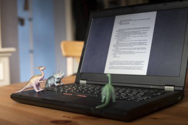 Seyir vasıl belgili tanımlık perde gibi görünüyor küçük dinozor oyuncakları ile ahşap masa üstünde açık laptop. Doğal ışık.