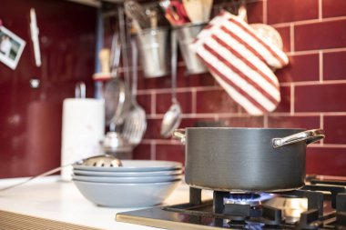 grey cooking pot on gas stove with steam releasing and blue dishes on the side in red burgundy classic kitchen with tools in the background.