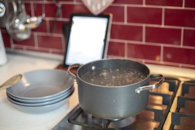 gaz pişirme tencere kaynar su, ahşap karıştırma kaşık ile mavi yemekleri ve tablet reçete ile yığını ile soba. Kırmızı mutfak içinde belgili tanımlık geçmiş.