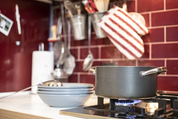 grey cooking pot on gas stove with steam releasing and blue dishes on the side in red burgundy classic kitchen with tools in the background.