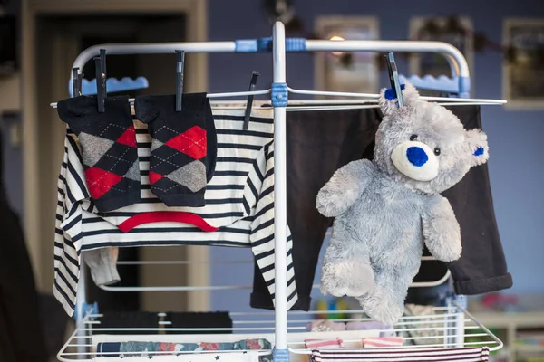 grey teddy bear plush toy hanging dry with laundry clothes after being washed. Front view.