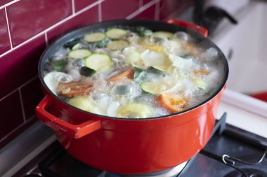 Ocakta, köpük ve kabarcıklar ile sebze çorbası kaynar ile kırmızı pot. Yan görünüm.